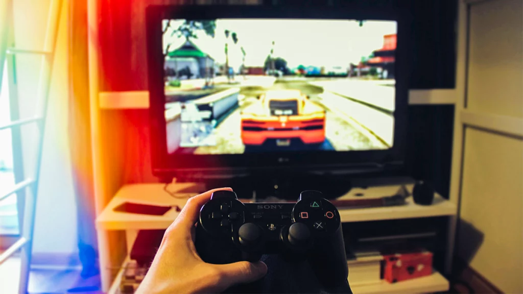 A person holds a PS4 controller, playing a racing video game on a TV screen